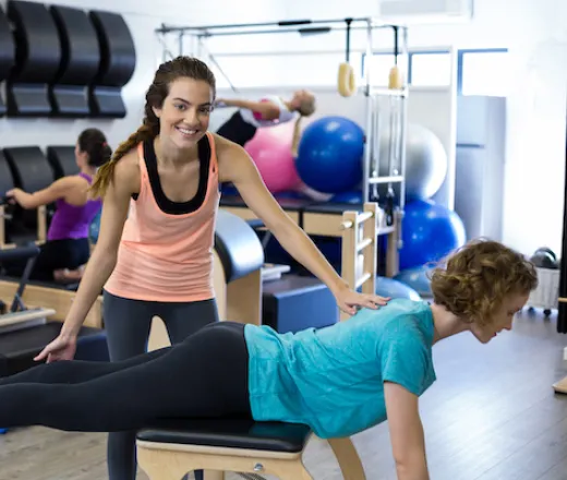 Female trainer assisting woman with stretching in Y Pilates Reformer